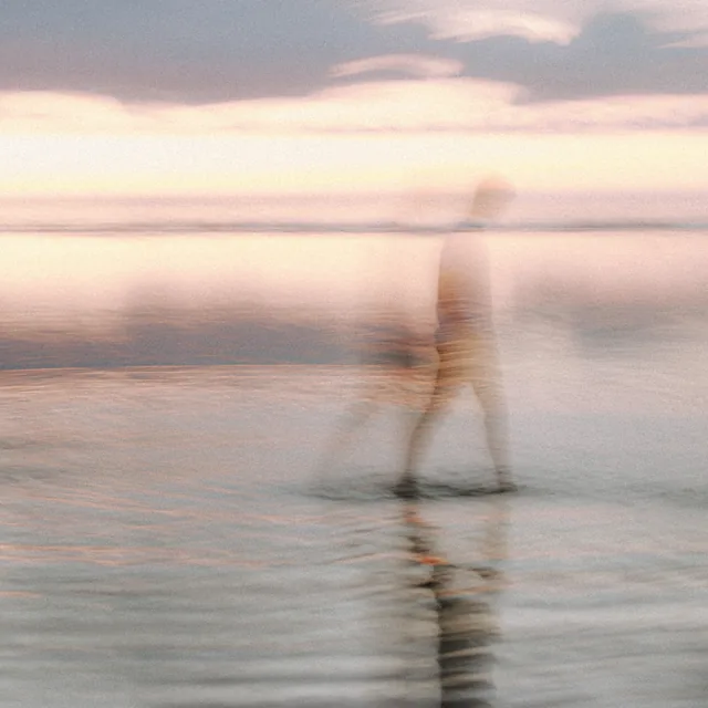 a lone figure walking the shallows at dusk